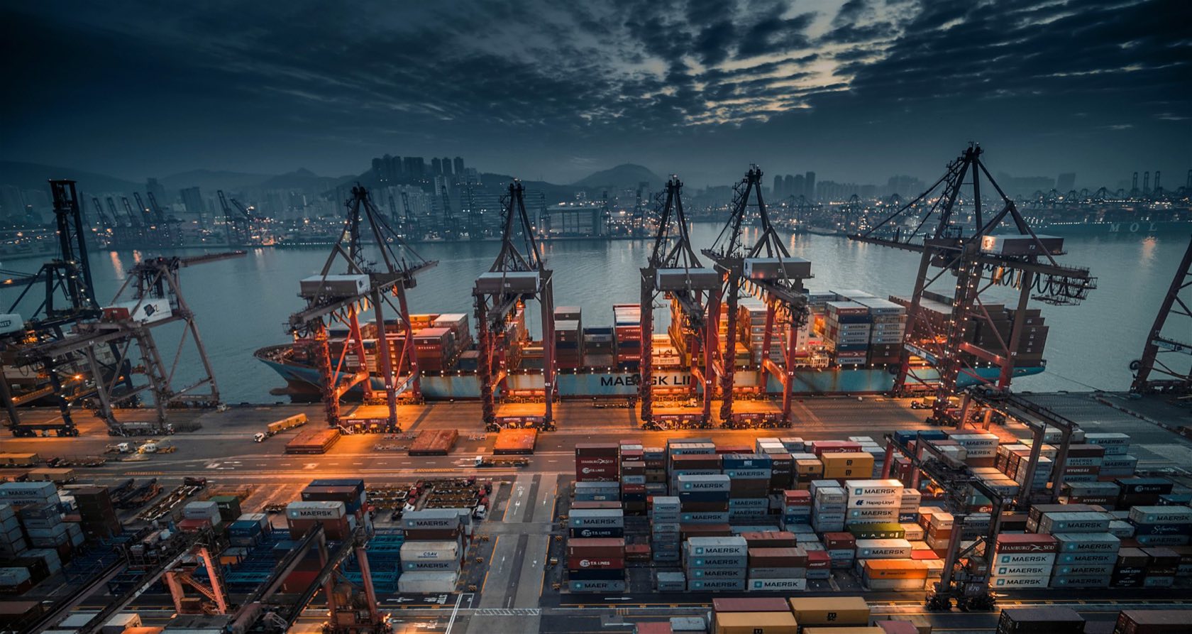 Container ship being loaded by gantry cranes at a port at dusk